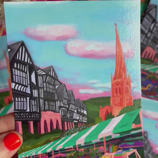 video of Postcard of an illustration of Chesterfield, Derbyshire town. Featuring the crooked spire, the Tudor buildings, the market, and the peak district hills. Set against a blue sky with fluffy white clouds. Designed by Rebecca Elizabeth Draws. 