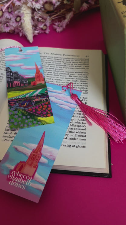 An illustration of chesterfield on a bookmark. A summer illustration featuring the famous crooked spire, market stalls and Tudor buildings. Soft blue sky with fluffy clouds, this art piece is a soft representation of the market town. The back features the same blue sky and clouds and a small crooked spire with the Rebecca Elizabeth draws logo. Designed by Rebecca Gibbs at Rebecca Elizabeth Draws.