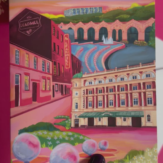 An illustrated greeting card of Sheffield city, Yorkshire. Featuring The Leadmill, the Lyceum, Sheffield train station, Sheffield Park Hill flats, park hill graffiti and water features. This illustration is very vibrant with bright pinks and oranges, the places featured are collaged together against a purple and orange sky. There is a small signature in white the corner.  Designed by Rebecca Gibbs at Rebecca Elizabeth Draws.
