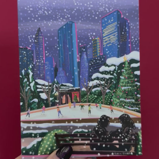Christmas Illustration inspired by the film Serendipity. The main stars are silhouetted at the front of this illustration with the new York skyline behind them, at the base of the high rise buildings are Christmas trees, the serendipity shop and an ice skate rink with people on. A christmas card with a blue back designed by Rebecca Gibbs at Rebecca Elizabeth Draws.