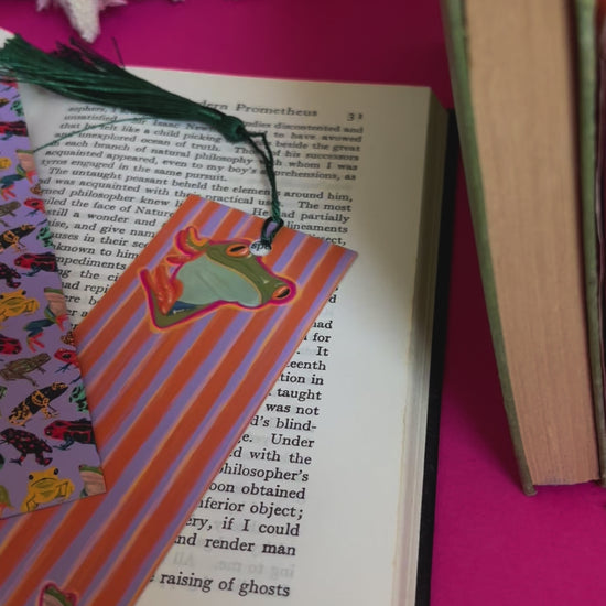 An illustration of frogs on a bookmark. A colourful frog pattern on a purple background on the front and a purple and orange stripe pattern on the back featuring some sneaky peak frogs alongside the Rebecca Elizabeth draws logo. Designed by Rebecca Gibbs at Rebecca Elizabeth Draws.