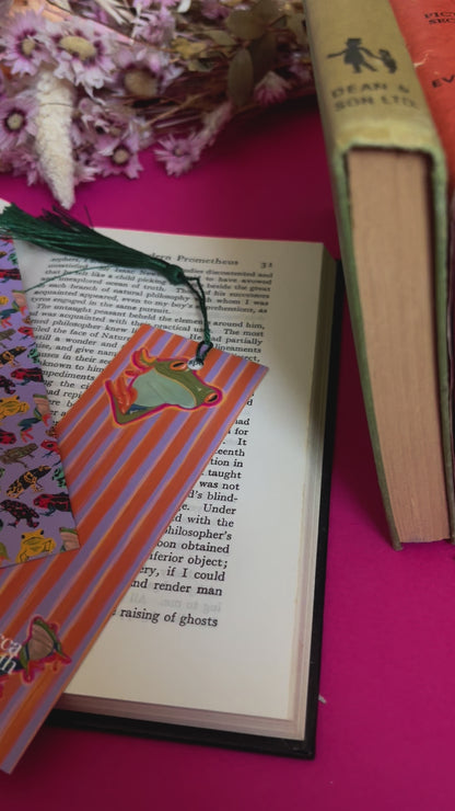 An illustration of frogs on a bookmark. A colourful frog pattern on a purple background on the front and a purple and orange stripe pattern on the back featuring some sneaky peak frogs alongside the Rebecca Elizabeth draws logo. Designed by Rebecca Gibbs at Rebecca Elizabeth Draws.