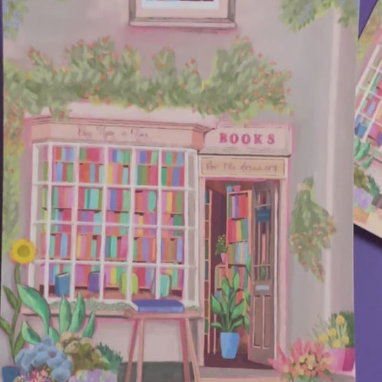 An illustration of a cute bookshop, the window shows the bookshelves inside full of bright coloured book spines. There are books placed stood up at the front. Outside the building is a soft colour with lots of greenery in soft pale greens and orange and lilac flowers. In front of the building there are plant pots and flowers. There is a small signature in white the corner.  Designed by Rebecca Gibbs on a postcard at Rebecca Elizabeth Draws.