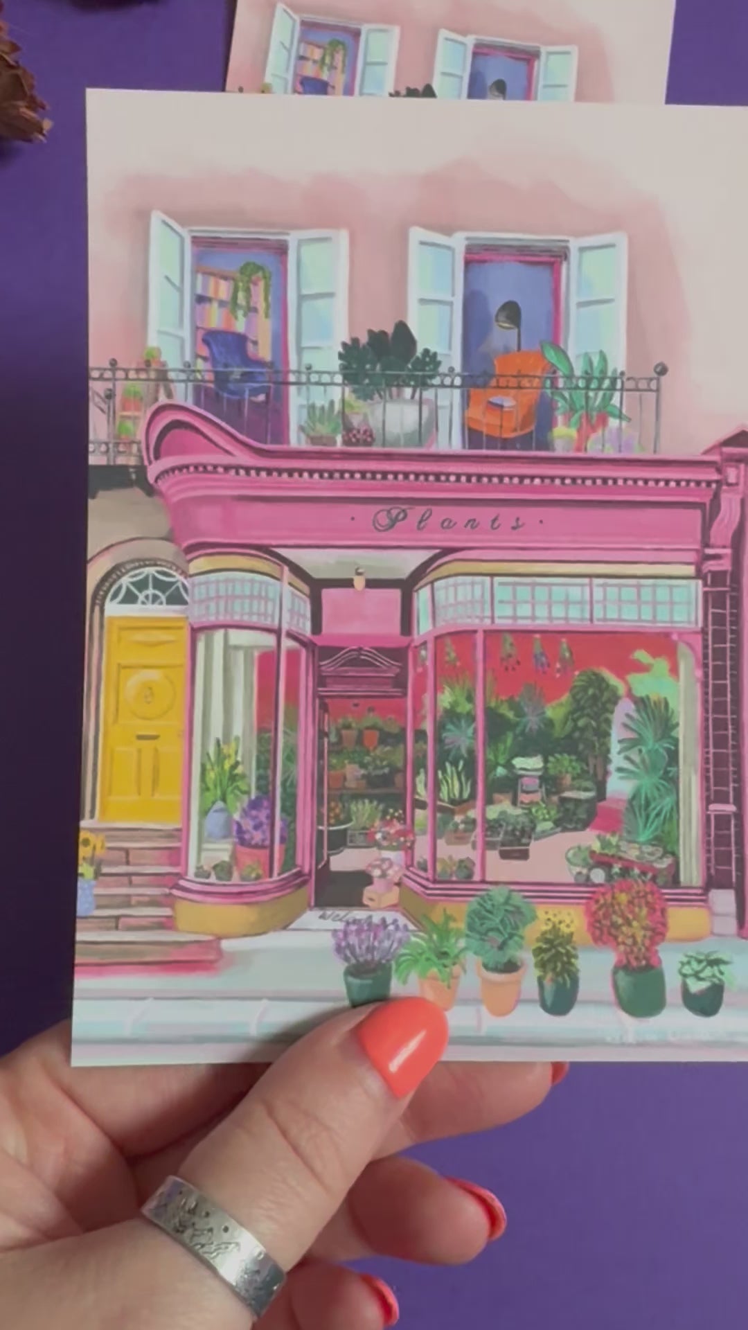 Pink shop front of a plant store with lots of greenery inside, a balcony above with windows showing chairs and a bookcase and more flowers. A yellow door to the side with a sunflower vase resting on the steps by Rebecca Elizabeth Draws. 