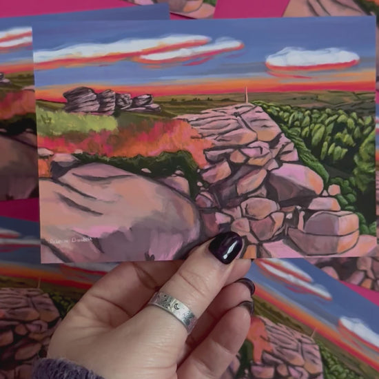 An illustrated postcard of Birchen Edge in the Peak District. With the rock face, rock outcrops named after ships from the battle of Trafalgar and Nelsons Monument all set against a sunset sky with blue, yellow, orange, and pink glow.