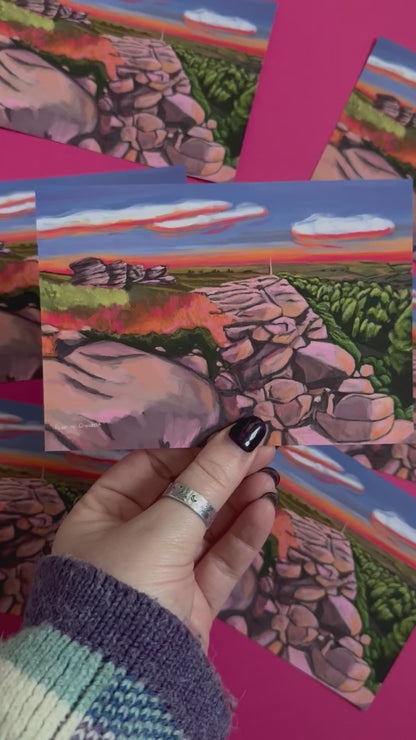 An illustrated postcard of Birchen Edge in the Peak District. With the rock face, rock outcrops named after ships from the battle of Trafalgar and Nelsons Monument all set against a sunset sky with blue, yellow, orange, and pink glow.